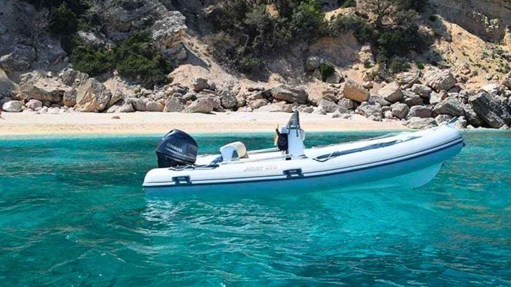 A white motorboat on clear turquoise water with a rocky shoreline in the background. 1