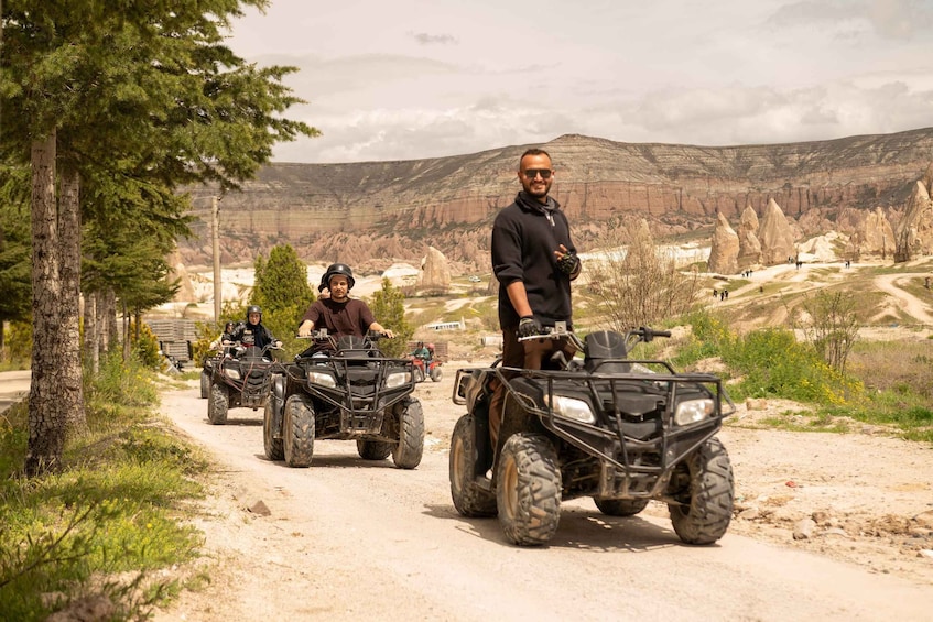 Eine Gruppe von Personen fährt mit Quads auf einem unbefestigten Weg, im Hintergrund eine gebirgige Landschaft. 5
