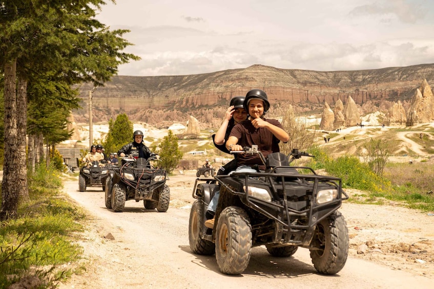 Eine Gruppe von Personen fährt mit Quads auf einer unbefestigten Straße vor einer gebirgigen Landschaft. 2