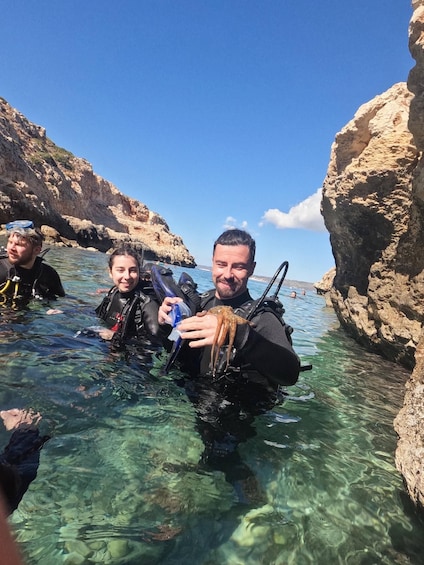 Divers in clear water with rocky cliffs, one holding a sea creature. 4