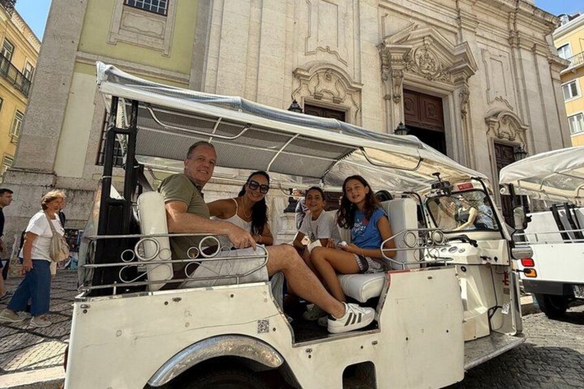 A white tour vehicle parked on a cobblestone street with tourists seated inside. 3