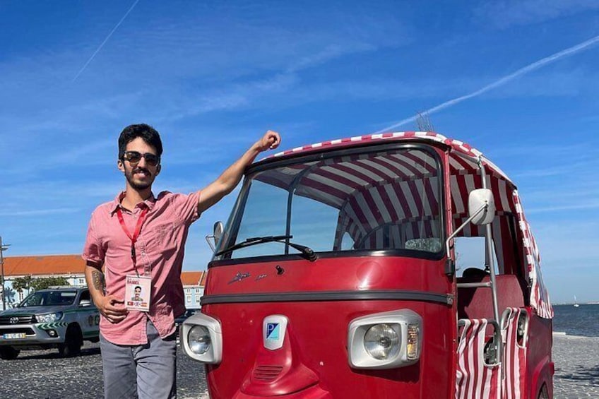 A red vehicle with a striped awning, a person standing next to it, and a body of water in the background. 5