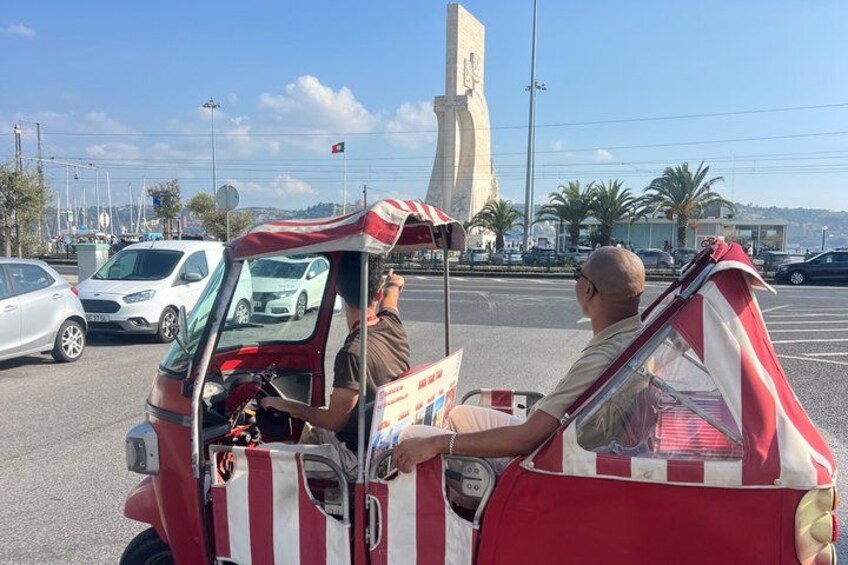A red and white striped vehicle with a canopy, parked in a parking lot with cars and a monument in the background. 5