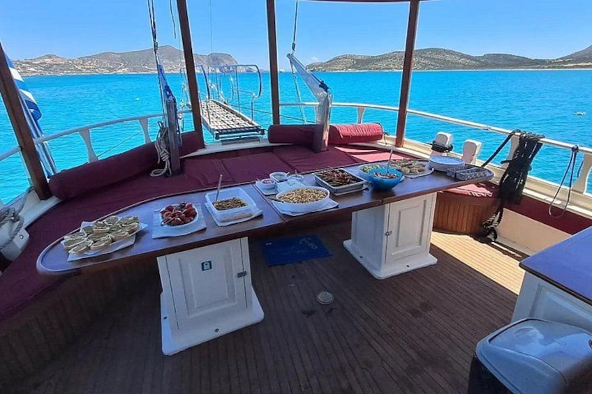 Een scheepdek met een gedekte tafel voor een maaltijd, omgeven door een prachtig uitzicht op zee en het land in de verte. 5