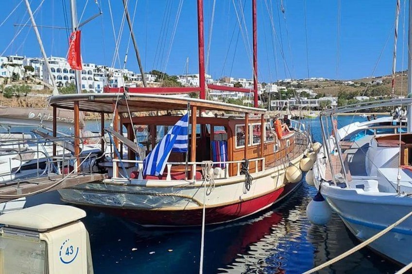 Een houten boot afgemeerd in een jachthaven, met andere boten, een heldere blauwe lucht en gebouwen op de achtergrond. 2