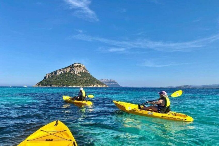Two people kayaking on clear blue water with a rocky island in the background. 2