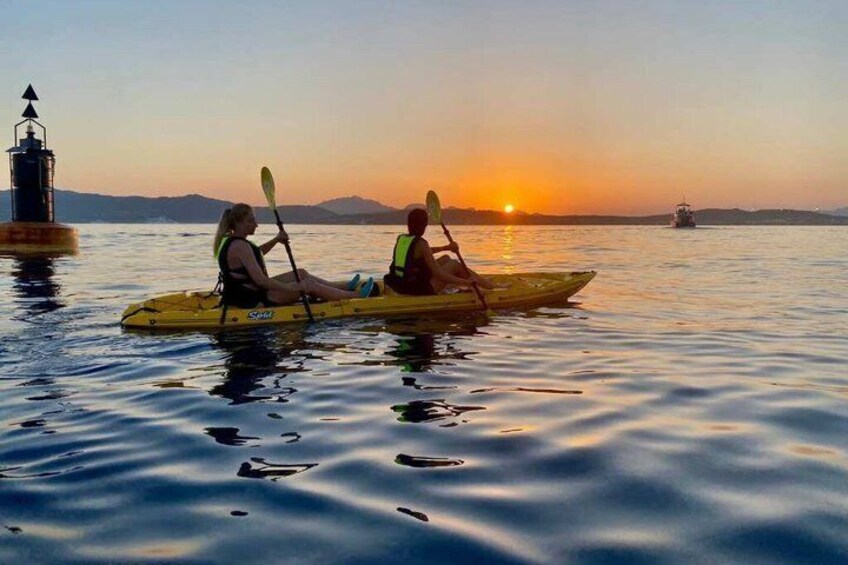 Two people kayaking on calm water during sunset with a lighthouse and a boat in the background. 3