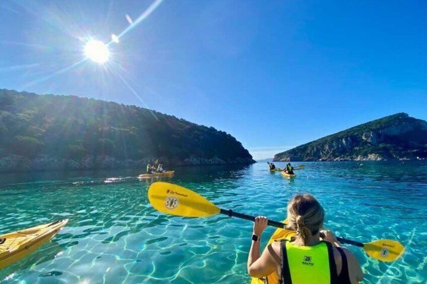 A kayaker in a clear blue sea with rocky cliffs in the background. 1