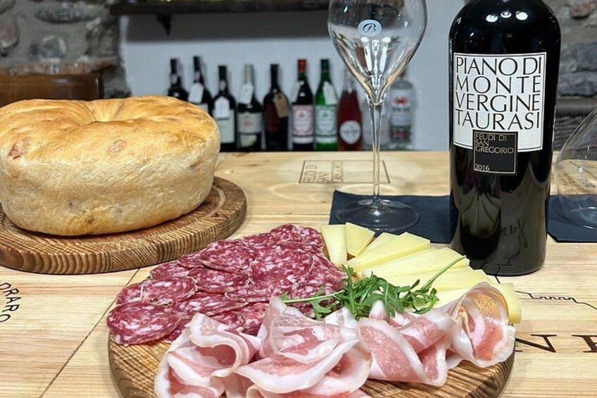 Una tabla de madera con varios embutidos, una hogaza de pan y una botella de vino. 1