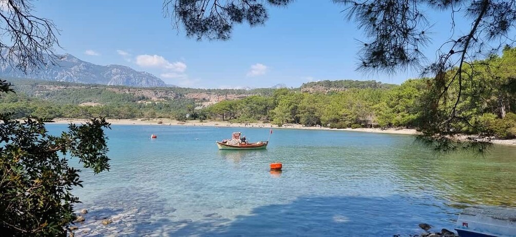 A calm lake with a boat, clear water, and a mountainous backdrop. 2