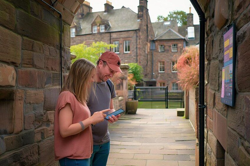 Two people standing in a stone-walled alleyway, one holding a smartphone. 5