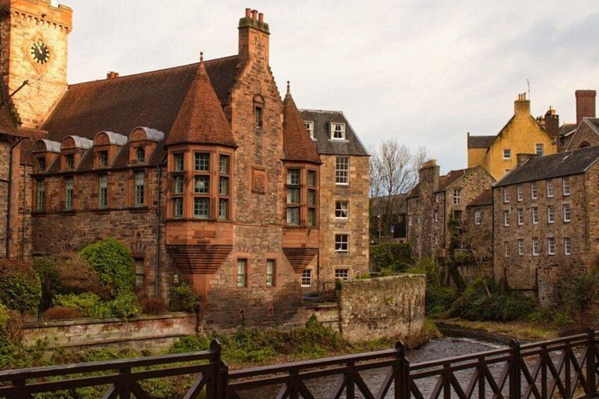 A historic stone building with a clock tower, surrounded by smaller buildings and a river. 4