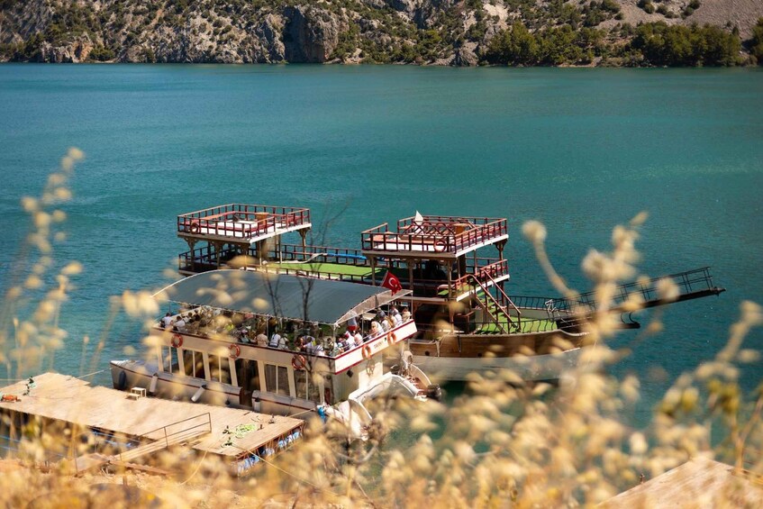 A ferry with multiple decks and passengers, docked at a pier with a mountainous backdrop. 4