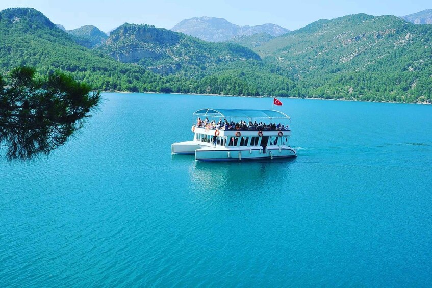 A boat with passengers on a turquoise lake surrounded by green hills. 5