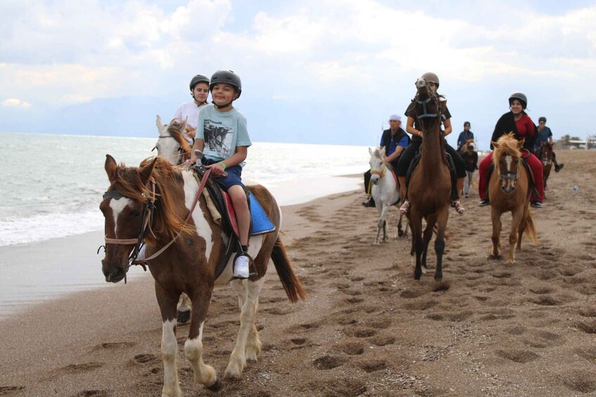 People riding horses along a beach with the ocean in the background. 1