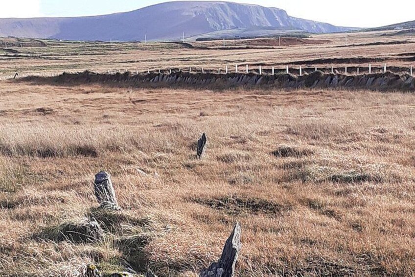 A grassy field with two stone cairns, a distant mountain, and a bridge in the background. 2