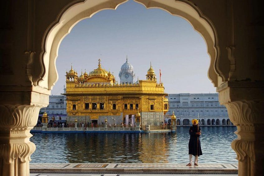The Golden Temple with a reflection in the water, surrounded by a white building and an archway. 4