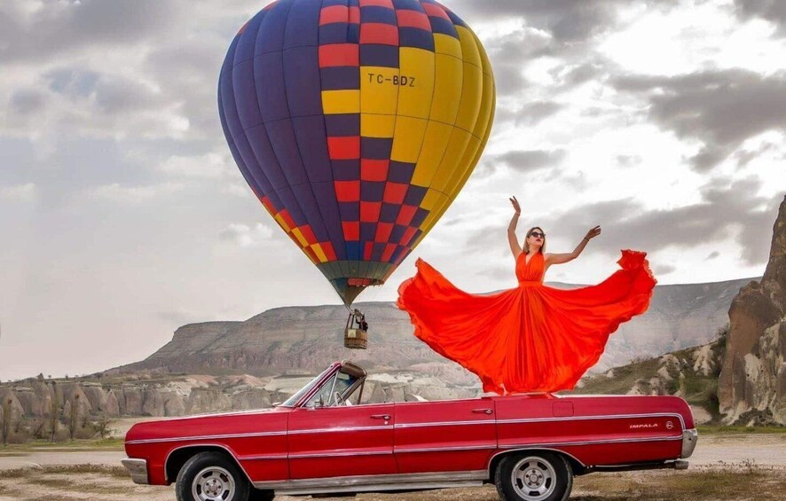 Un descapotable rojo con una mujer vestida de rojo, un globo aerostático y un paisaje montañoso. 4