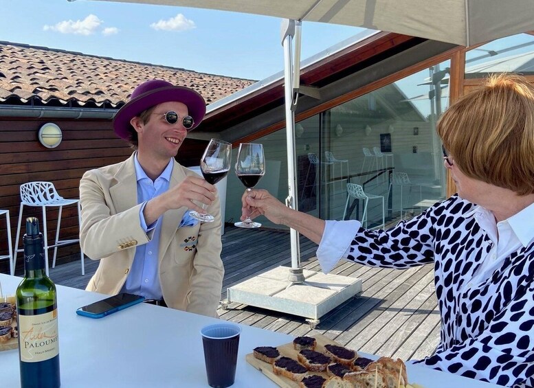 Two people toasting with wine glasses at an outdoor table with a bottle of wine and snacks. 4