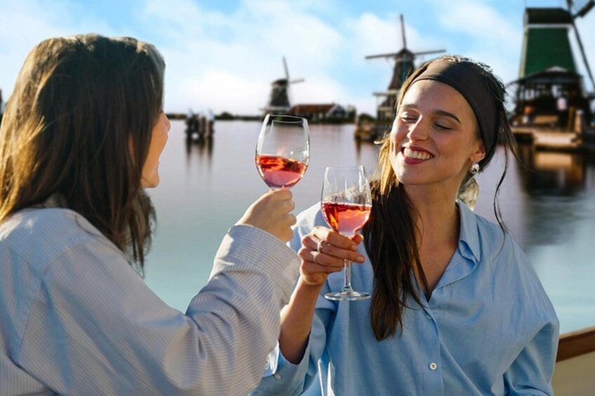 Two people toasting with wine glasses, a calm body of water, and windmills in the background. 3