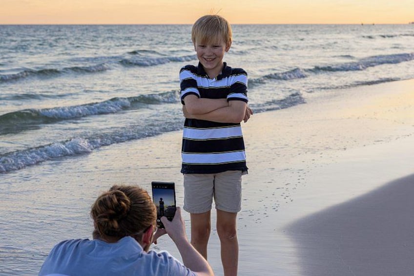 En person tager et billede af en anden person, der står på en strand med bølger i baggrunden. 3