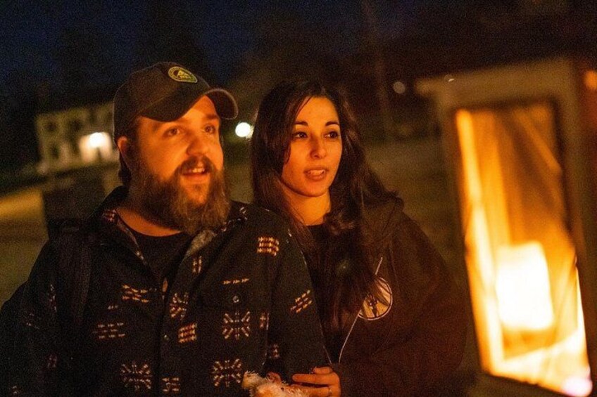 Two people standing outdoors at night with artificial lighting. 1