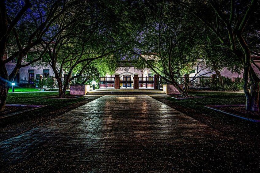 A paved pathway leading to a building with arched windows, surrounded by trees and illuminated by artificial lighting. 2