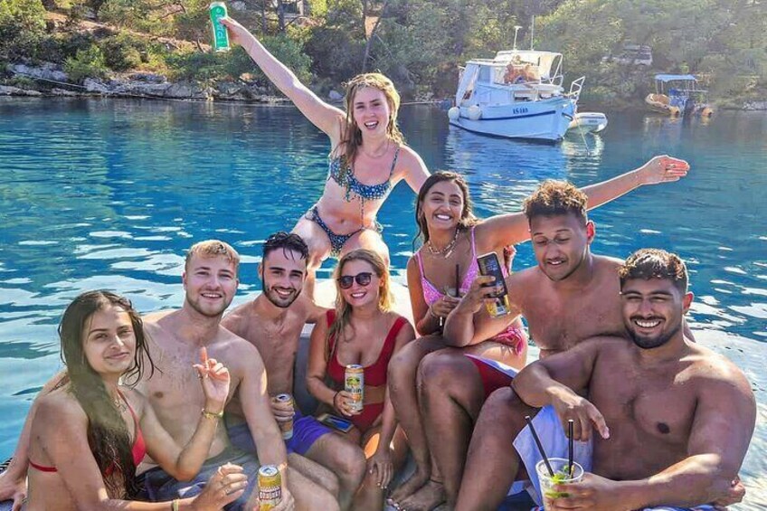 A group of people on a boat in a body of water with a boat docked in the background. 1