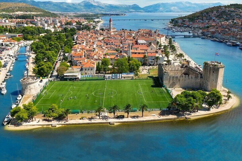 An aerial view of a coastal city with a historic fort, a large green sports field, and a harbor with boats. 3