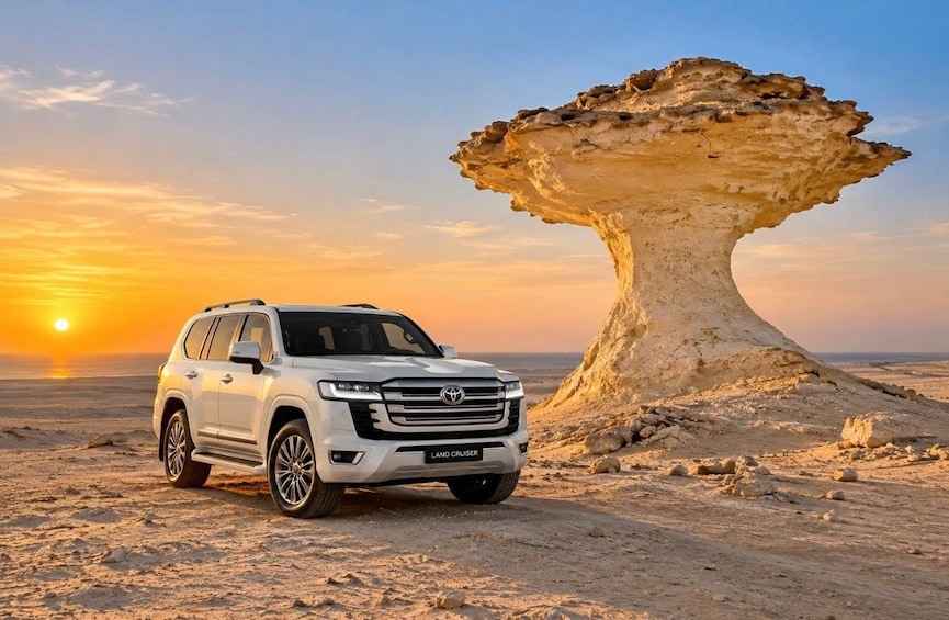 Un SUV bianco parcheggiato su un paesaggio desertico con un'insolita formazione rocciosa sullo sfondo. 1