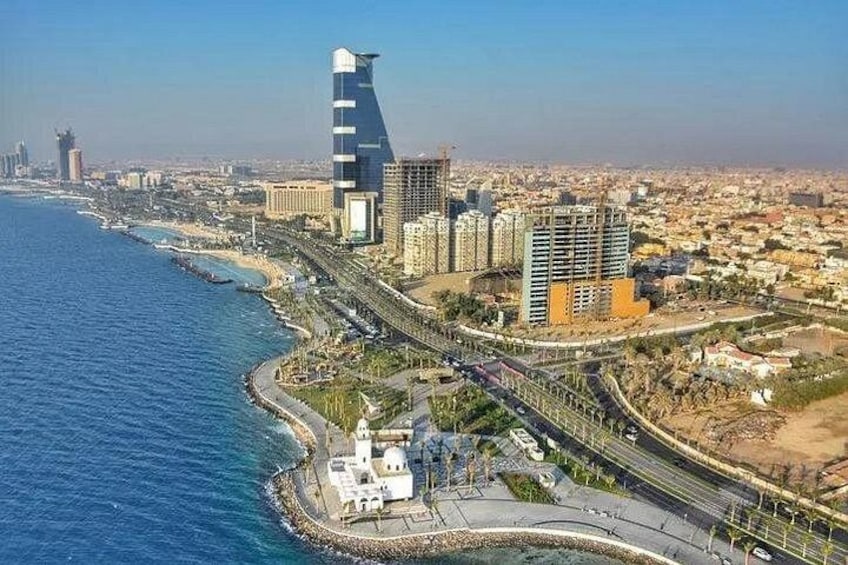 A coastal cityscape with a prominent curved skyscraper, a highway, and a beach. 1