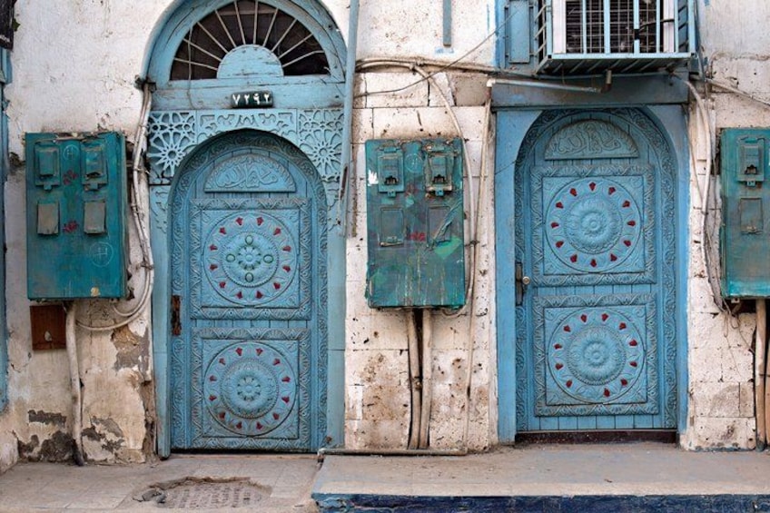 Dos puertas azules ornamentadas con detalles intrincados, frente a una fachada de edificio desgastada por el tiempo. 3