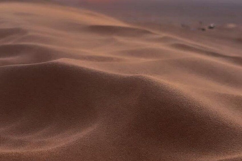 Een detailopname van zandduinen met rimpelingen en een verre blik op een woestijnlandschap. 2
