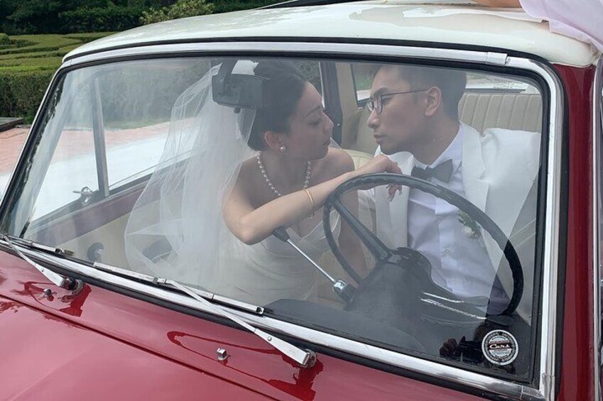 Een rode oldtimer met een wit dak, een man en een vrouw in bruidsoutfit. 2
