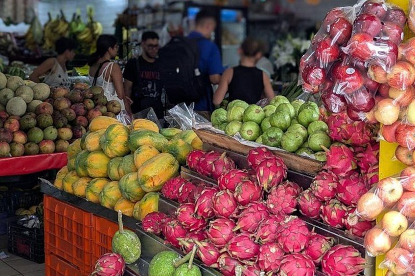 En fruktmarknad med ett varierat utbud av frukter, som till exempel drakfrukt, äpplen och bananer. 2