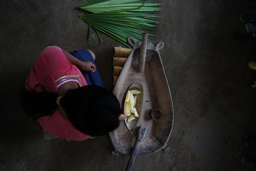A person kneeling on the ground, peeling ginger with a knife, and a bunch of green onions nearby. 2