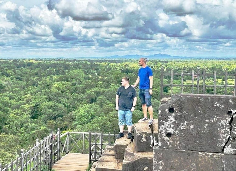 Two people standing on a stone platform with a view of a forested landscape. 2