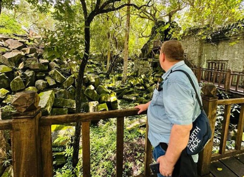 A person standing on a wooden bridge in a forested area with a stone wall and lush greenery. 5
