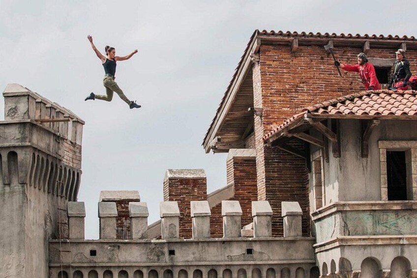 A person jumping off a building, another person on the roof, and a historic building with arches. 1