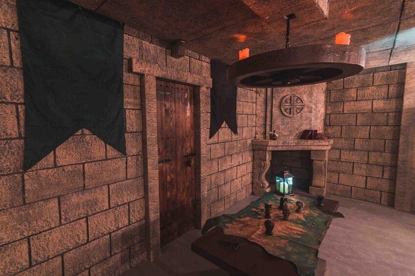 A stone-walled room with a fireplace, a table with chess pieces, and a hanging tapestry. 5