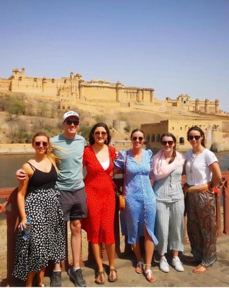 A group of people standing on a bridge with a historic fort in the background. 1