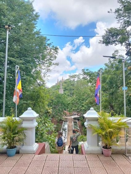 A pathway leading to a temple complex surrounded by lush greenery and two flags on poles. 2
