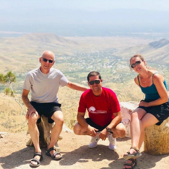 Three people sitting on a rock with a mountainous landscape in the background. 1