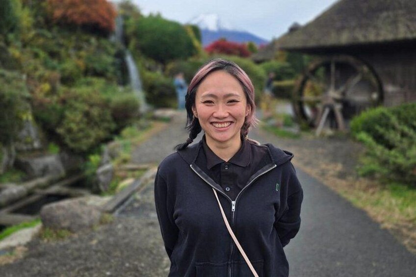 A person standing on a path with a thatched-roof structure and a water wheel in the background. 3