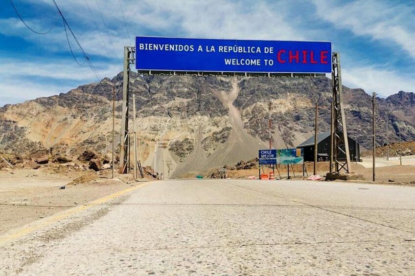 A road leading to a mountainous area with a sign welcoming visitors to Chile. 2