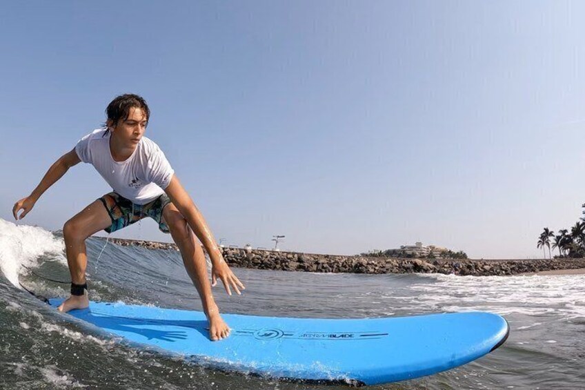 A person surfing on a blue board with a rocky shoreline and palm trees in the background. 4