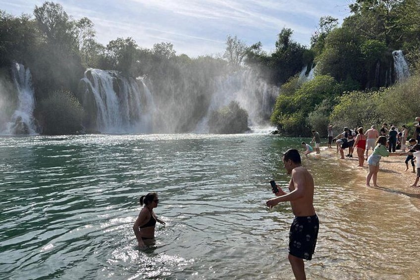 A waterfall, people swimming, and a sandy beach. 1