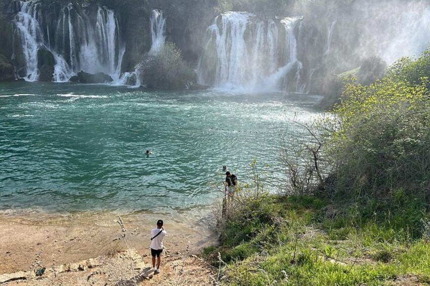 A waterfall, a river, and two people standing on a cliff overlooking the water. 2