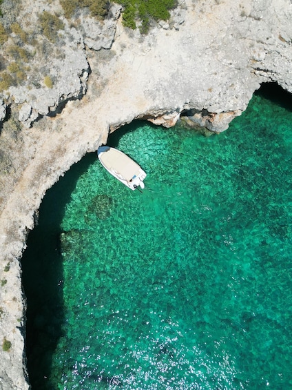 A boat in a clear turquoise sea, partially sheltered by a rocky cave. 1