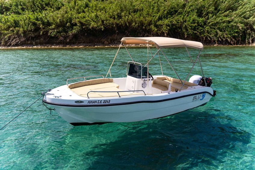 A small white motorboat with a canopy, anchored in clear blue water with a rocky shoreline in the background. 5